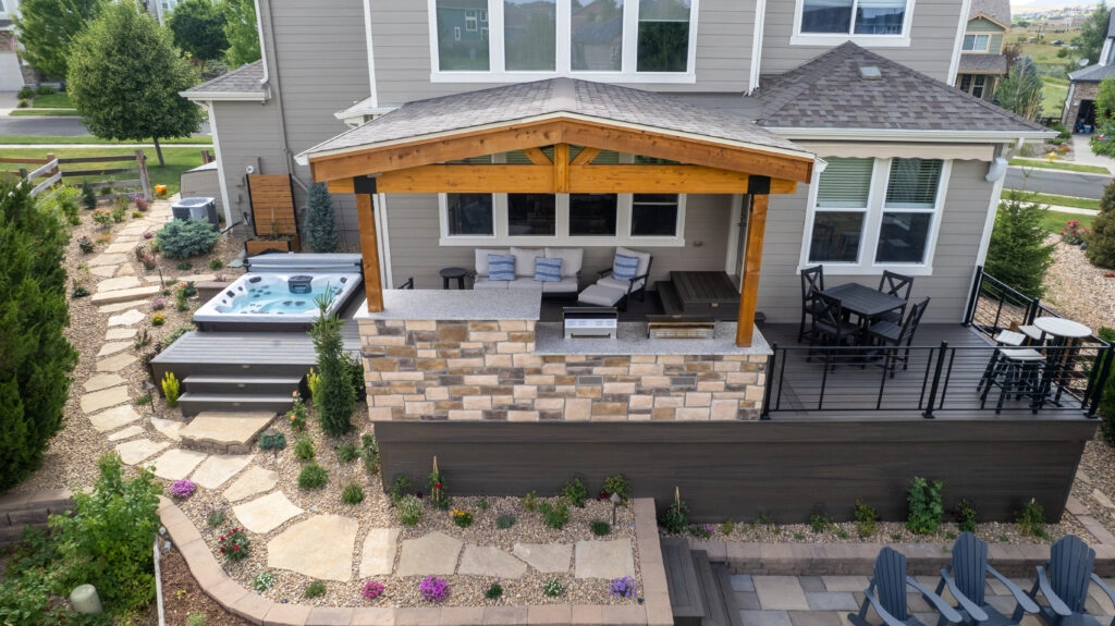 Aerial view of a backyard with a covered patio, composite deck, hot tub, and flagstone landscaping