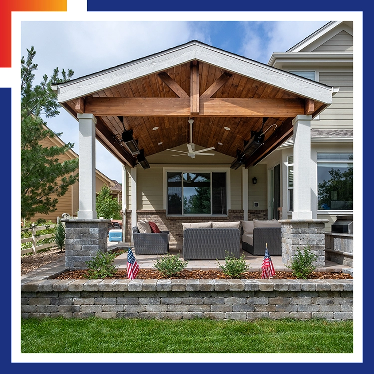 Covered patio with an exposed timber gable roof, wicker seating, and a stacked stone retaining wall