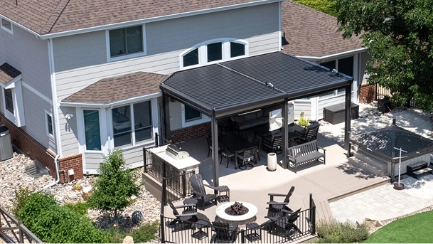 Aerial view of a freestanding Azenco louvered pergola over a backyard patio with a dining set, fire pit, and hot tub