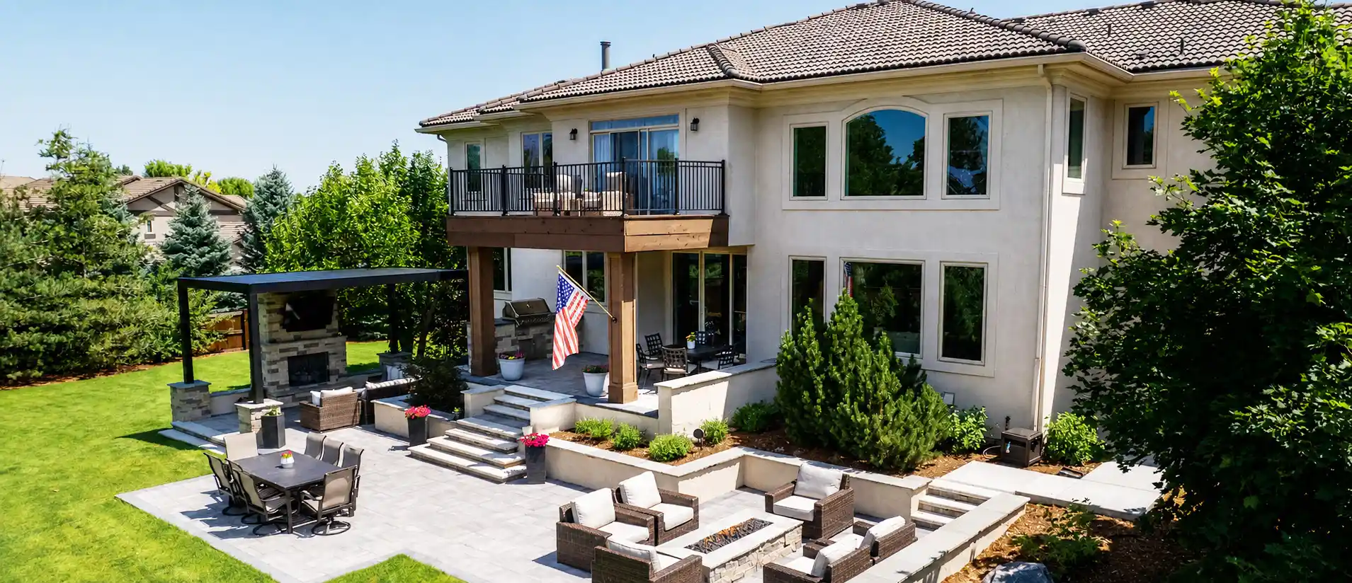Landscaped backyard with a paver patio, stone fire pit, outdoor kitchen, and covered pergola